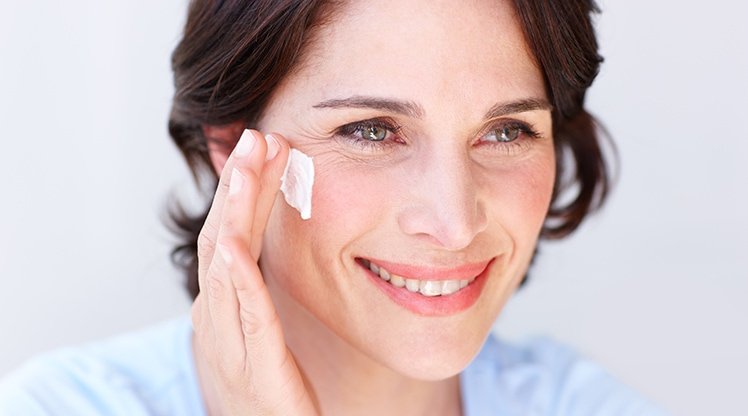 Eine Frau trägt Creme auf ihre rechte Wange auf